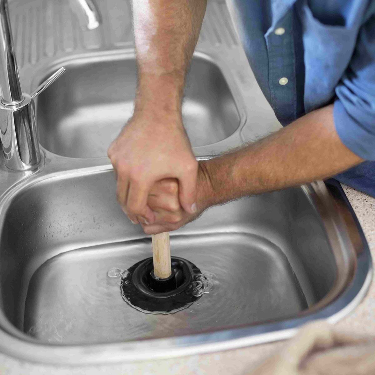 Manos usando un desatascador en el fregadero de una cocina durante una intervención en Vigo