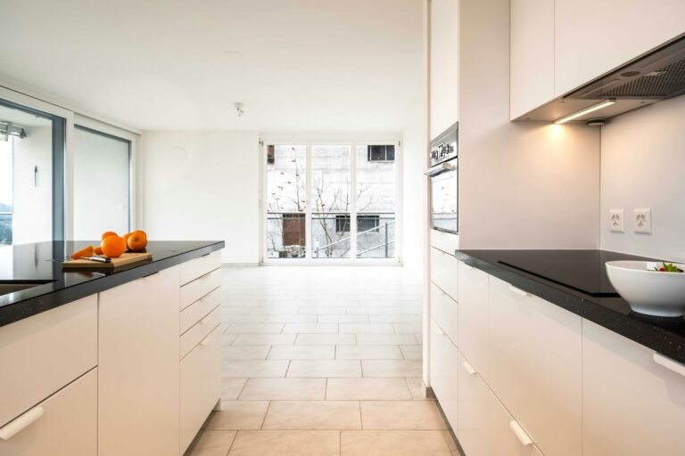 Cocina reformada con muebles blancos y encimera oscura en un piso de Granada