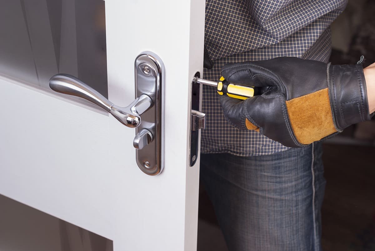 Cerrajero ajustando con un destornillador la cerradura de una puerta